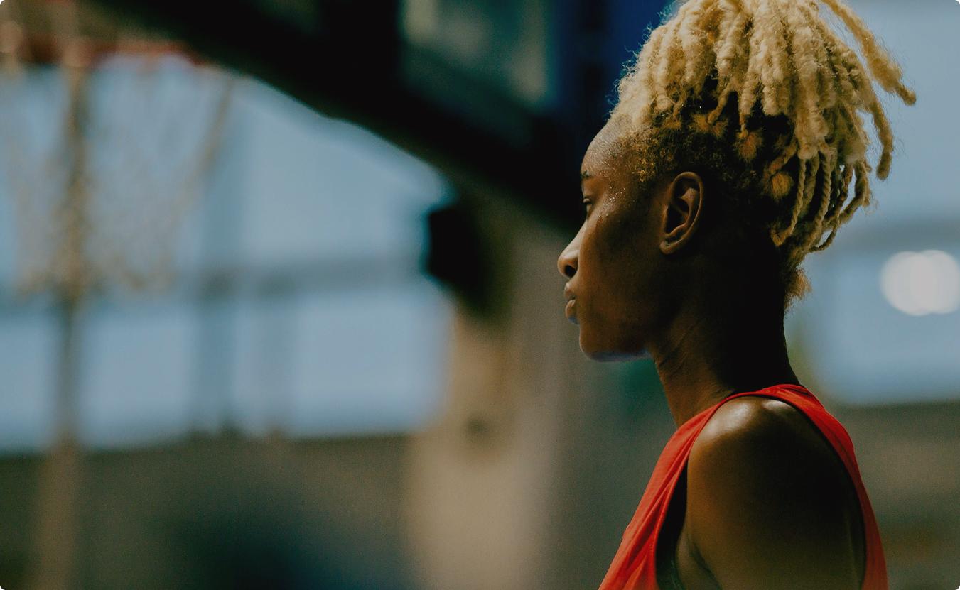 Image of a female athlete standing in a red top standing in a sports court, the background has been slightly blurred.