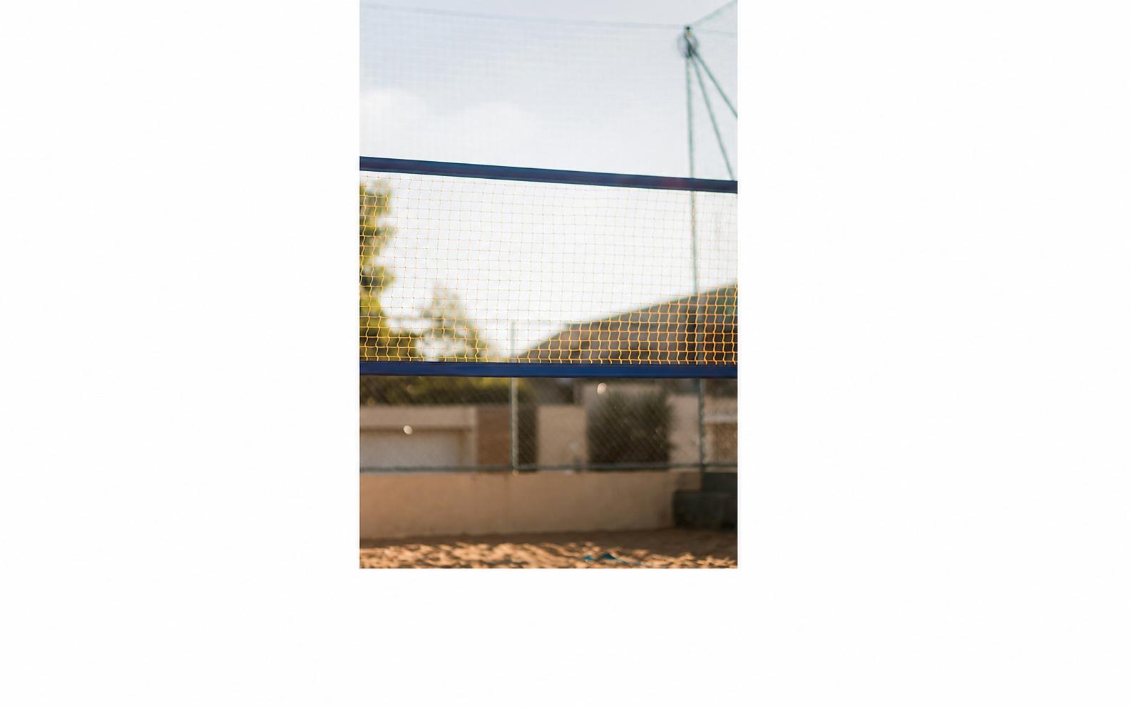 A volleyball net and beach background is seen