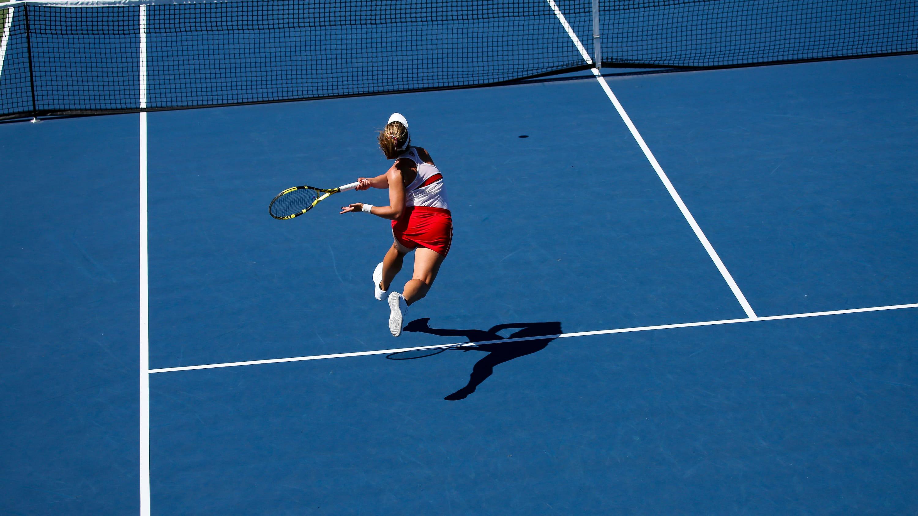 A tennis player wearing red and white is seen mid shot on a blue tennis court